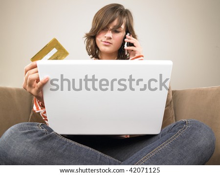Young woman with laptop, holding credit card and talking on the phone. Vertically framed shot.