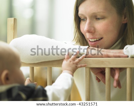 Mom Smiling at Baby Over Playpen Railing. Horizontally framed shot.