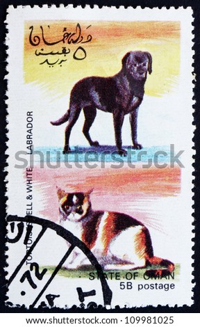 OMAN - CIRCA 1972: a stamp printed in the Oman shows Tortoiseshell and White Cat And Labrador Dog, circa 1972