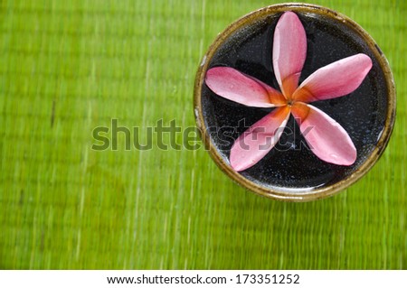 Pink frangipani flower in bowl on straw mat