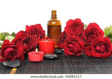 Set of red rose and massage oil and candle with stones on bamboo mat