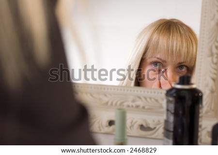 Blonde woman making makeup of her face in front of mirror before working day