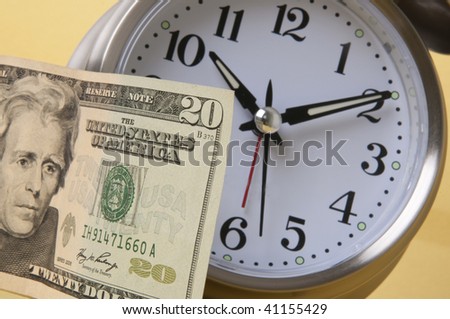 In today's world time is money.  Alarm clock and American paper currency isolated on a yellow background.