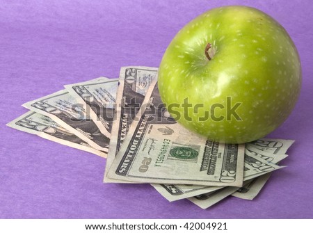 A green apple sits on top of a pile of $20 bills to illustrate the cost of education, food, or health care.