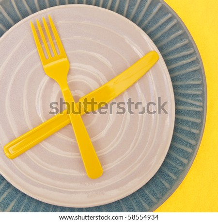 Modern Place Setting with Empty Plate and Plastic Yellow Silverware on Yellow Background.
