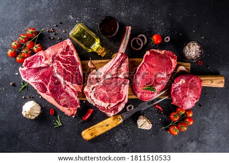 Set of various classic, alternative raw meat, veal beef steaks - chateau mignon, t-bone, tomahawk, striploin, tenderloin, new york steak. Flat lay top view on black stone cutting table