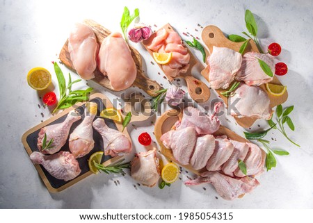 Various raw chicken meat portions. Set of uncooked chicken fillet, thigh, wings, strips and legs on white cooking table background with spices 