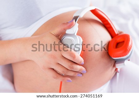 Pregnant woman playing music for baby by the headphones