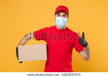 Delivery man employee in red cap blank t-shirt uniform face mask gloves hold empty cardboard box isolated on yellow background studio Service quarantine pandemic coronavirus virus 2019-ncov concept