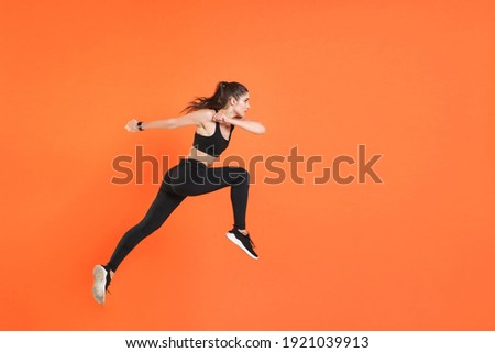 Full length side view of portrait of young fitness sporty woman 20s wearing black sportswear posing training working out jumping like running looking aside isolated on orange color background studio Foto d'archivio © 