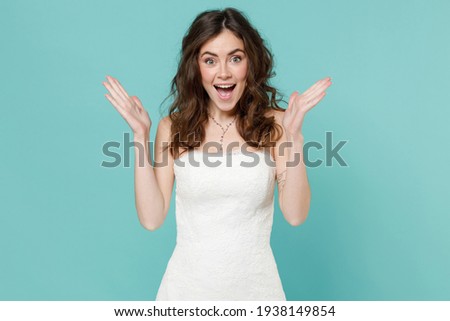 Surprised tender bride young woman 20s in beautiful white wedding dress spreading hands keeping mouth open isolated on blue turquoise background studio portrait. Ceremony celebration party concept