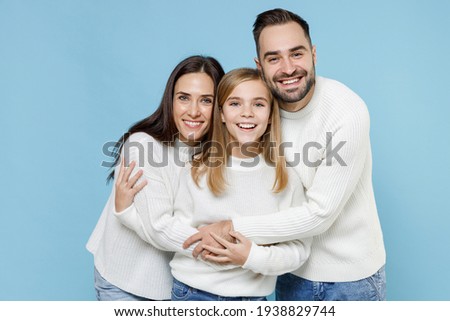 Laughing fun young happy parents mom mama dad papa with child kid daughter teen girl in white sweaters hugs isolated on blue color background studio portrait. Family day parenthood childhood concept