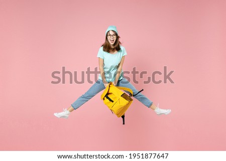 Full length portrait of excited young woman student in t-shirt hat glasses hold backpack jumping spreading legs isolated on pink background studio. Education in high school university college concept Foto d'archivio © 