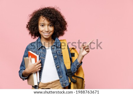 Smiling little smart african kid school girl 12-13 years old in casual clothes backpack hold books point index finger aside on copy space isolated on pastel pink background Childhood education concept