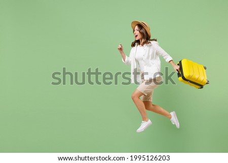 Full length traveler tourist woman in casual clothes straw hat jump high hold suitcase run isolated on pastel green background. Passenger travel abroad on weekends getaway. Air flight journey concept