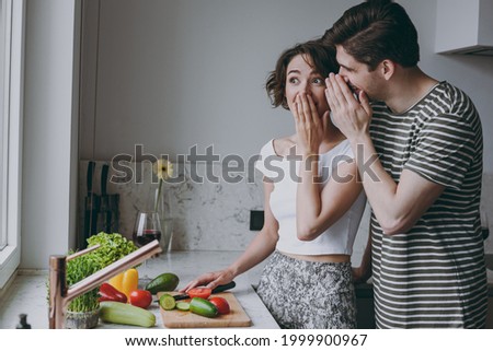 Young shock couple two woman man 20s in casual clothes boyfriend whisper gossip and tells secret behind his hand sharing news cook food in light kitchen at home together Healthy diet lifestyle concept Foto stock © 
