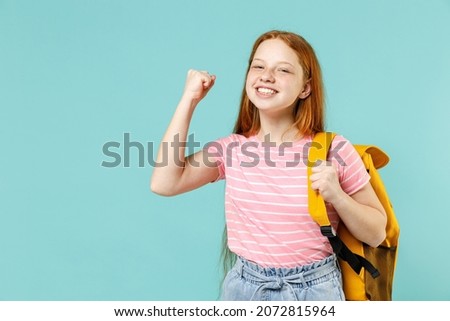 Little overjoyed pupil redhead kid girl 12-13 year old in pink t-shirt yellow school bag backpack do winner gesture clench fist isolated on pastel blue background Children lifestyle childhood concept Stock foto © 