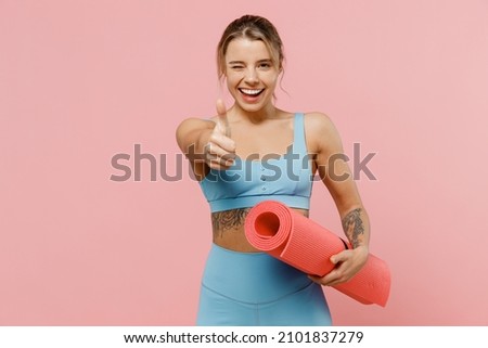 Young strong sporty athletic fitness trainer instructor woman wear blue tracksuit spend time in home gym show thumb up gesture blink isolated on pastel plain pink background. Workout sport concept. Foto stock © 
