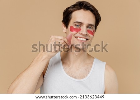 Young man 20s perfect skin in undershirt wearing pink patch under eye doing face massage hold rose quartz guache scrape isolated on light pastel beige background Skin care cosmetic procedures concept Foto stock © 