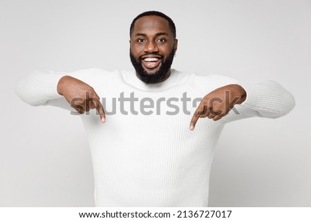Funny cheerful smiling young african american man 20s wearing casual basic sweater standing pointing index fingers down on mock up copy space isolated on white color wall background studio portrait Foto stock © 