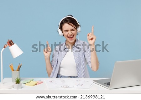 Young secretary employee business woman in casual shirt sit work at white office desk with pc laptop wearing headphones listen to music resting during break isolated on pastel blue background studio Foto stock © 