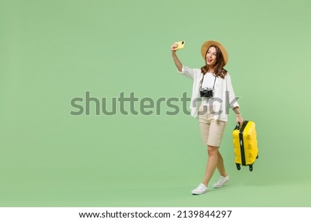 Full length traveler tourist woman in casual clothes hat hold suitcase do selfie on mobile cell phone isolated on pastel green background. Passenger travel abroad weekends. Air flight journey concept Stock foto © 