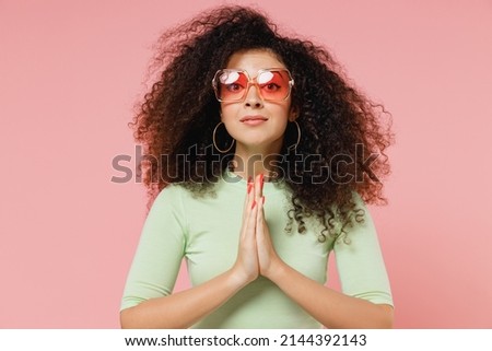 Pleading young curly latin woman 20s years old wears mint t-shirt sunglasses hands folded in prayer gesture begging about something wait isolated on plain pastel light pink background studio portrait Imagine de stoc © 