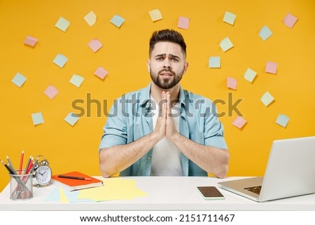 Young asking pleaded employee business man in shirt sit work at white office desk with pc laptop hands folded in prayer gesture, begging about something isolated on yellow background studio portrait. Imagine de stoc © 