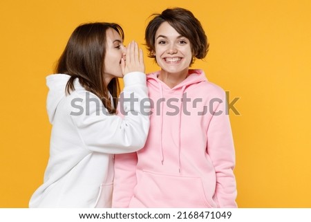 Smiling funny two young women friends 20s in casual white pink hoodies whispering gossip and tells secret behind her hand, sharing news isolated on vivid bright yellow color background studio portrait Foto stock © 