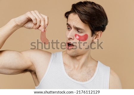 Young sad man he 20s perfect skin in undershirt wear pink patch under eye do face massage hold rose quartz guache scrape isolated on plain pastel beige background Skin care cosmetic procedures concept Foto stock © 