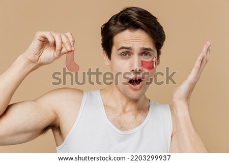 Young confused man he 20s perfect skin in undershirt wear patch under eye do face massage hold rose quartz guache scrape isolated on plain pastel beige background Skin care cosmetic procedures concept Foto stock © 