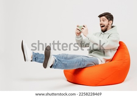 Full body young gambling man in mint hoody sit in bag chair use play racing app on mobile cell phone hold gadget smartphone for pc video games isolated on plain solid white background studio portrait Photo stock © 