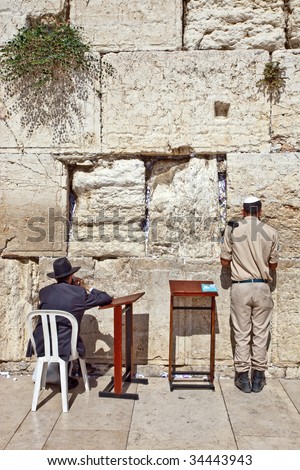 An Israeli soldier intensely prays at the Western Wall while an ultra-Orthodox man talks on his cellphone
