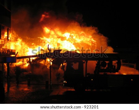 The silhouette of a firetruck with a burning house in the background