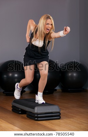 Beautiful blond young woman performing step aerobics exercise in a gym
