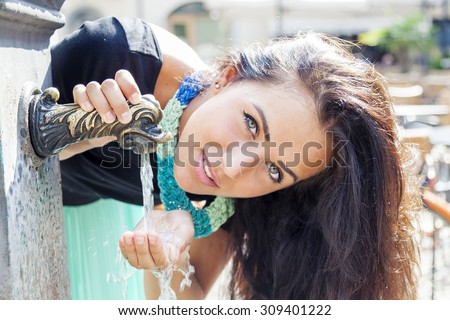 portrait of pretty girl drinks water from source in summer city