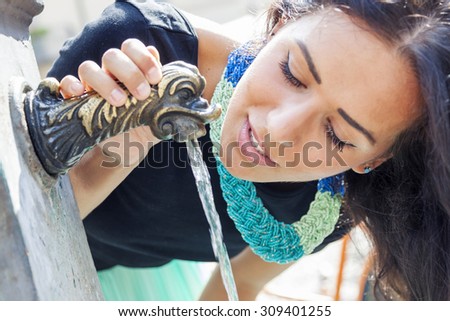 portrait of pretty girl drinks water from source in summer city