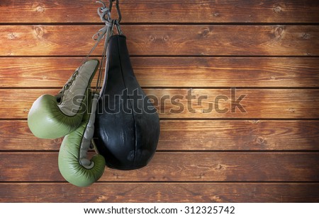 old boxing gloves and punching bag hang on wooden background