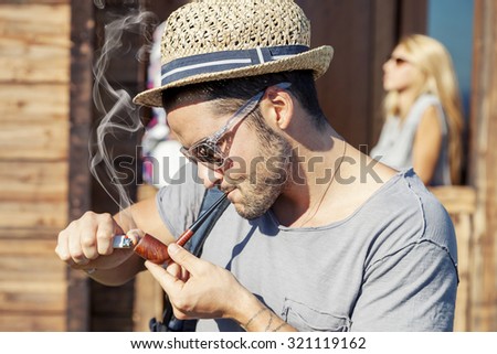 young hiker lights his pipe in front of the hut