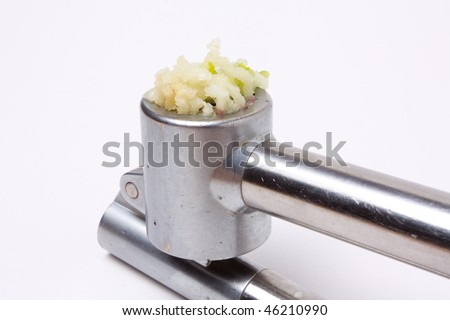 Crushed garlic oozing from a shiny silver garlic press isolated against white background.
