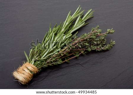 Bunches of Rosemary and Thyme bound with string against dark slate background.