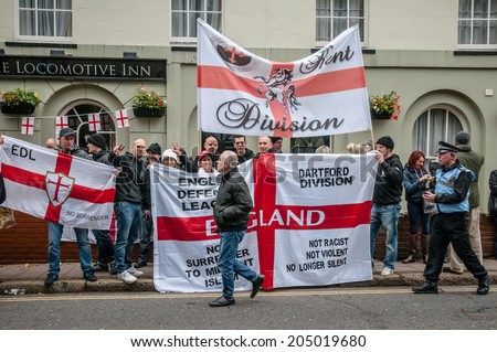 EXETER, UK - NOVEMBER 16: English Defence League supporters hold up flags will a man walks passed during the English Defence League march and rally November 16, 2013 in Exeter, Devon, UK