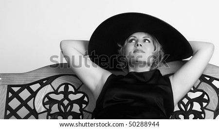 close-up portrait of a woman in black dress and wide-brimmed hat siting on a bench