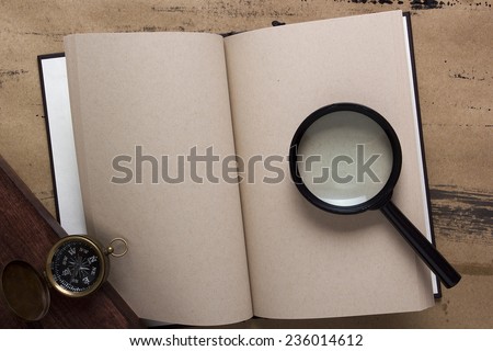 Old book with blank pages, compass and magnifying glass.