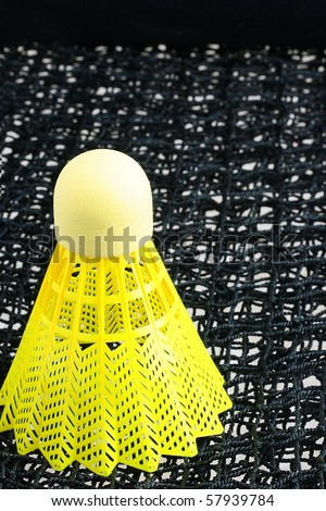 A bright yellow badminton shuttlecock on a black badminton net.