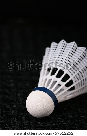 Close-up of a white synthetic shuttlecock on a black badminton net.