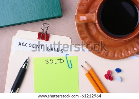 A manila account sales folder laying next to a cup of coffee and office supplies.
