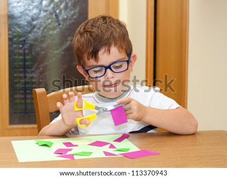 Child with glasses cutting paper with scissors