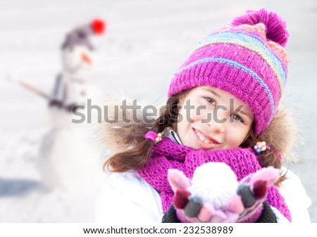 Girl wearing hat, scarf and mittens doing a snowman