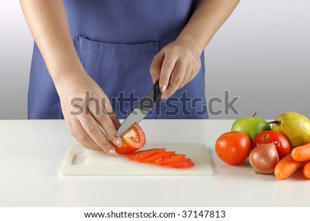 A woman slicing tomatoes with some fruits and vegetables on the side